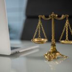 Golden justice scales on a desk beside a laptop, symbolizing law and balance.