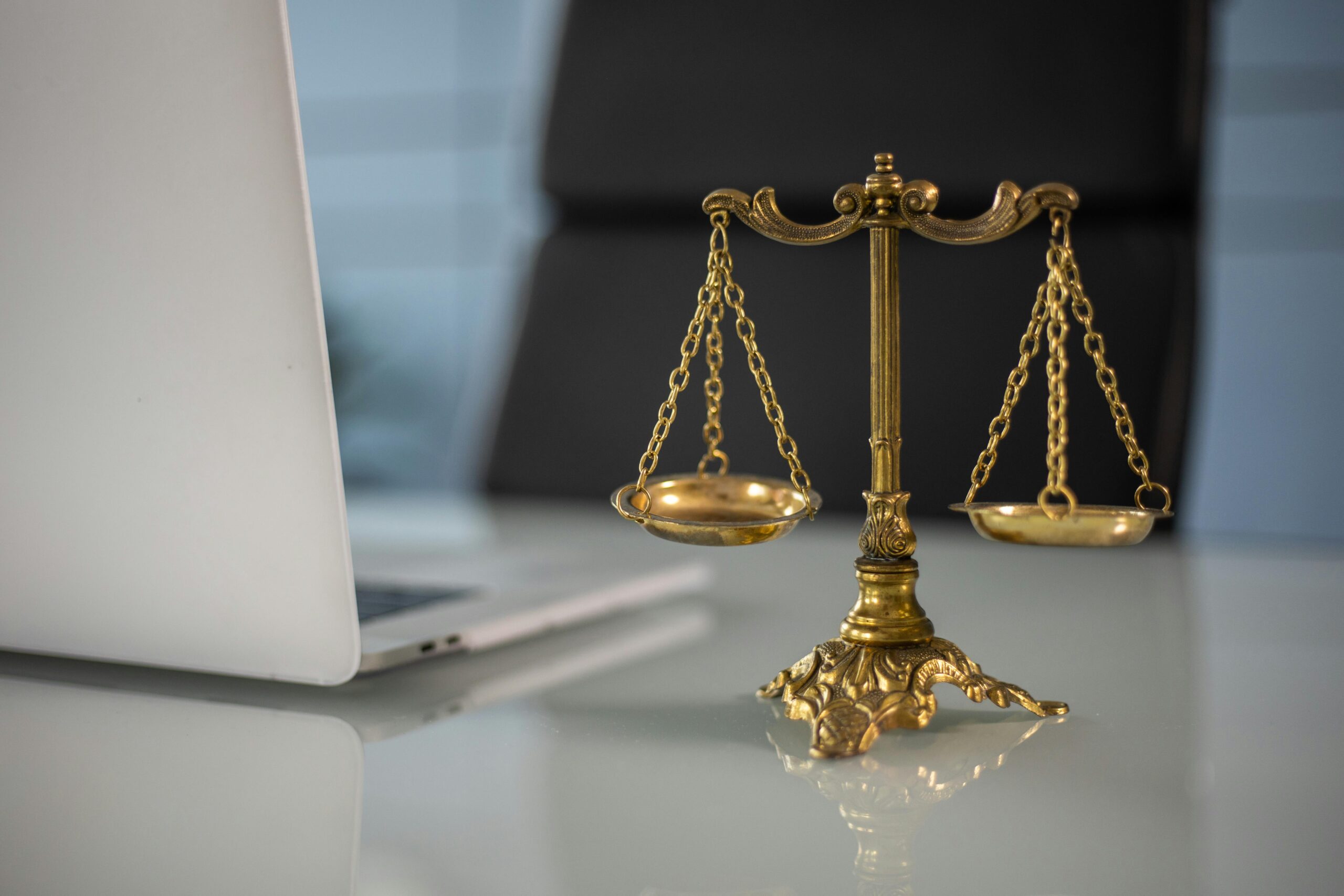 pexels photo 6077797 6077797 Golden justice scales on a desk beside a laptop, symbolizing law and balance.